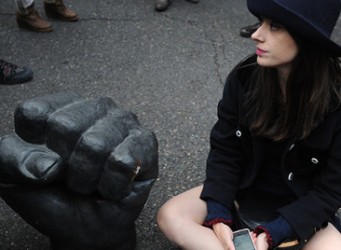 una mujer sentada en el suelo junto a una escultura que representa un puño cerrado
