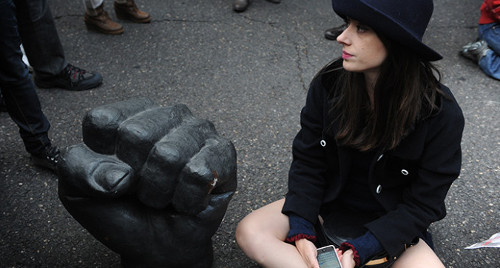 una mujer sentada en el suelo junto a una escultura que representa un puño cerrado