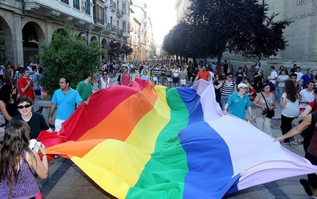 Personas portando una gran bandera arcoiris