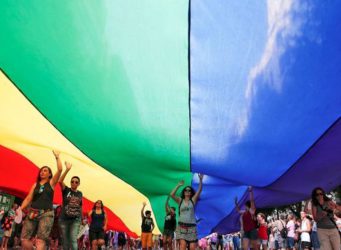 Imagen de participantes en una manifestación con una enorme bandera arco iris