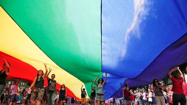 Imagen de participantes en una manifestación con una enorme bandera arco iris