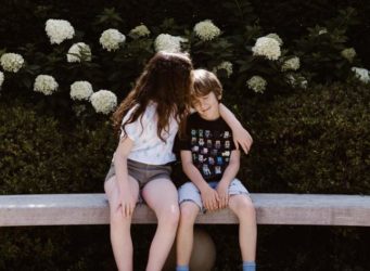 una niña le da un beso a un niño sentados en un banco