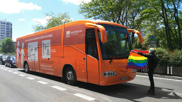 Imagen de una activista con una bandera arcoiris delante del bus de Hazte Oir