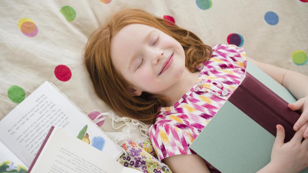 una niña con un libro en las manos y los ojos cerrados sonriente