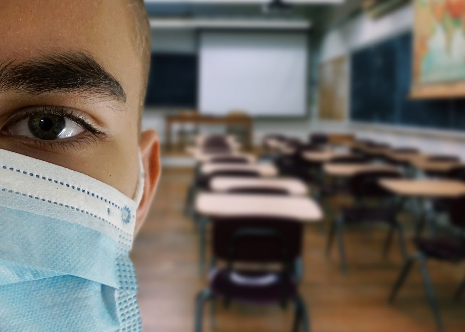 un joven con mascarilla ante una clase vacía