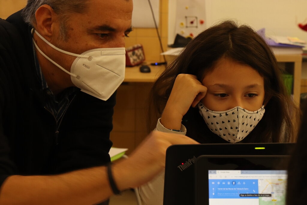 una niña y un adulto con mascarillas miran pantallas