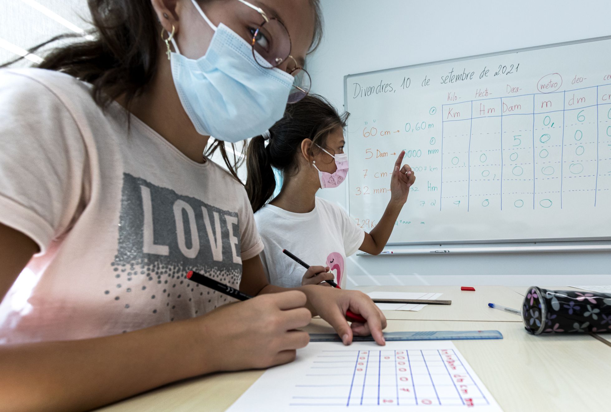 dos niñas con mascarilla estudian en una mesa