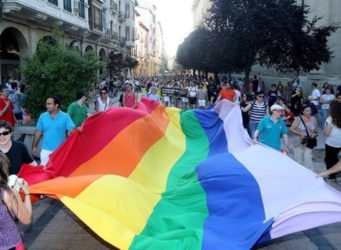 Personas portando una gran bandera arcoiris