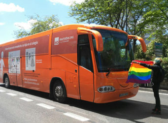Imagen de una activista con una bandera arcoiris delante del bus de Hazte Oir