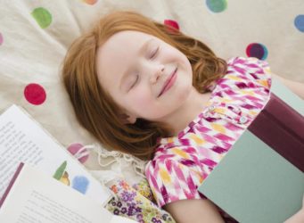 una niña con un libro en las manos y los ojos cerrados sonriente