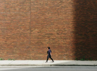 una mujer camina delante de un muro de ladrillo